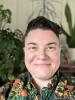 A white masculine person with short hair and a green floral shirt smiles towards the camera.